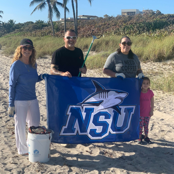 NSU alumni holding up an NSU banner at a beach clean-up event